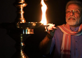 Unity against COVID-19: Wrapping an Assamese Gamocha around his neck PM Modi lights diya for India