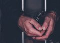 Handcuffed man behind prison bars