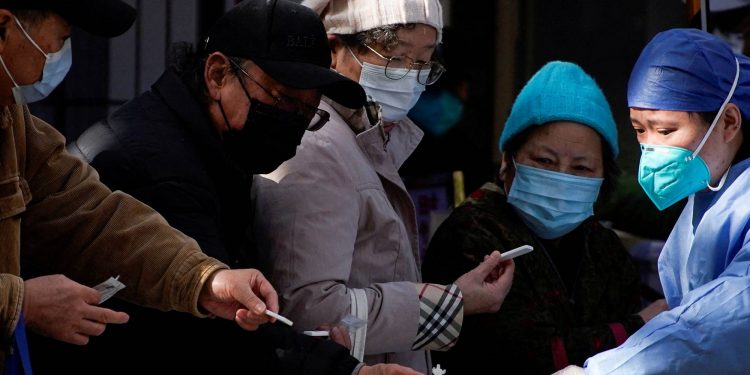 A medical worker in a protective suit checks rapid antigen tests for Covid-19 at an entrance of a hospital, as coronavirus disease (COVID-19) outbreaks continue in Shanghai, China, December 13, 2022. REUTERS/Aly Song